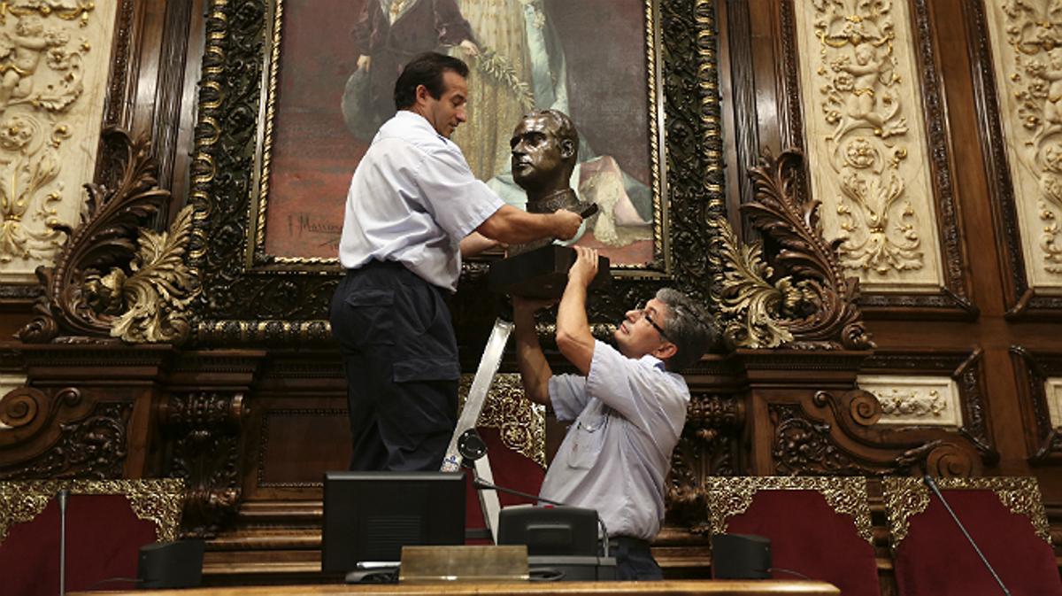 Dos operarios retiran el busto del rey Juan Carlos del salón de plenos del Ayuntamiento de Barcelona.