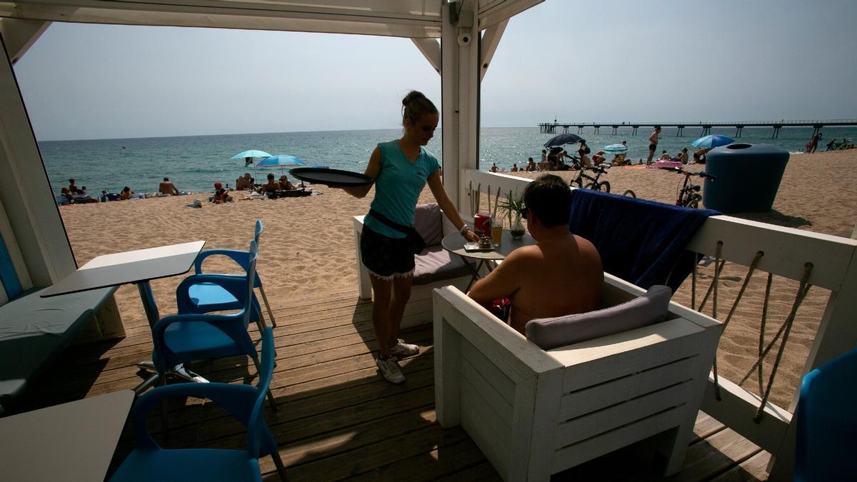 La tasa de paro en España cae al 12,48%. En la foto, una camarera atiende a un cliente en un chiringuito de la playa de Barcelona.