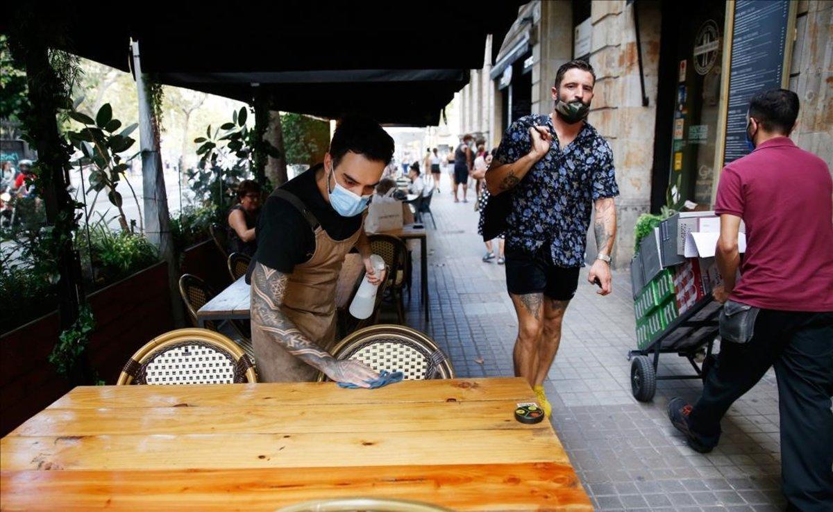 Un trabajador de un bar de Barcelona limpia una mesa de la terraza del local.