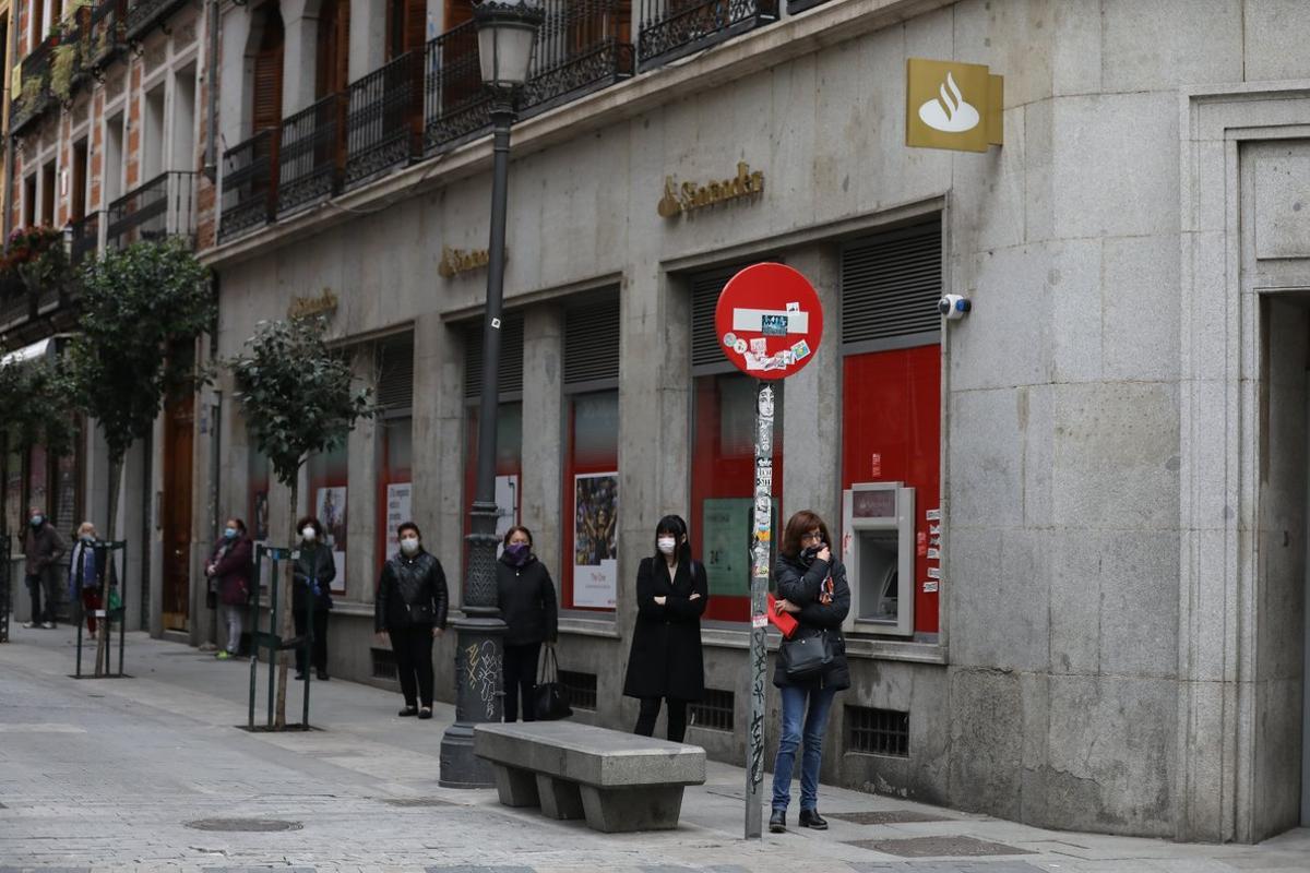 Varias personas esperan en una cola con distancia de seguridad para entrar en una sucursal del Banco Santander en Madrid.