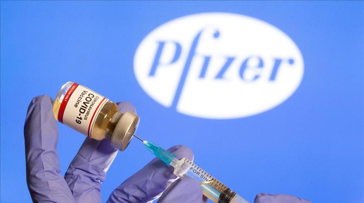 Una mujer sostiene una pequeña botella etiquetada con una etiqueta adhesiva de vacuna contra el coronavirus y una jeringa médica frente al logotipo de Pfizer.