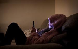 Una adolescente mirando el móvil en el sofá de su casa.