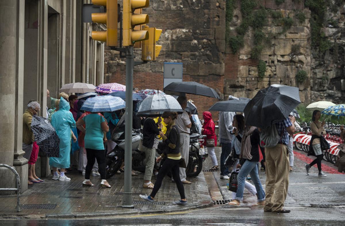 Diversos ciutadans es protegeixen de la pluja, aquest diumenge a Barcelona.