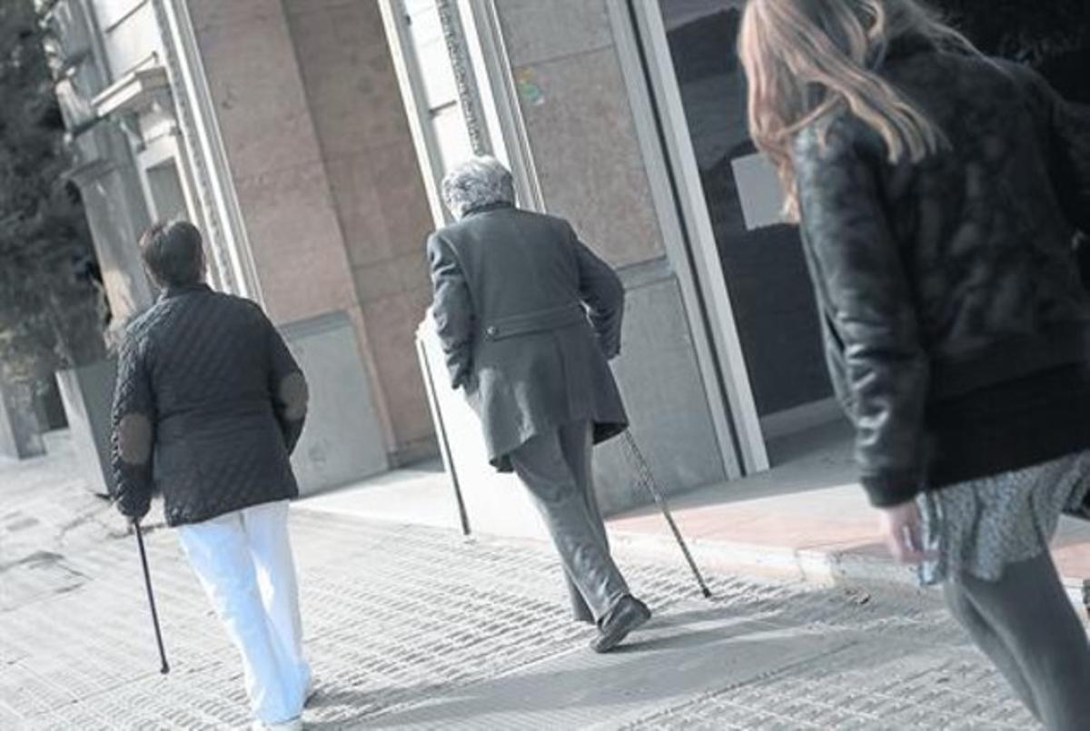 Una anciana y su cuidadora andan  por una calle de Barcelona.