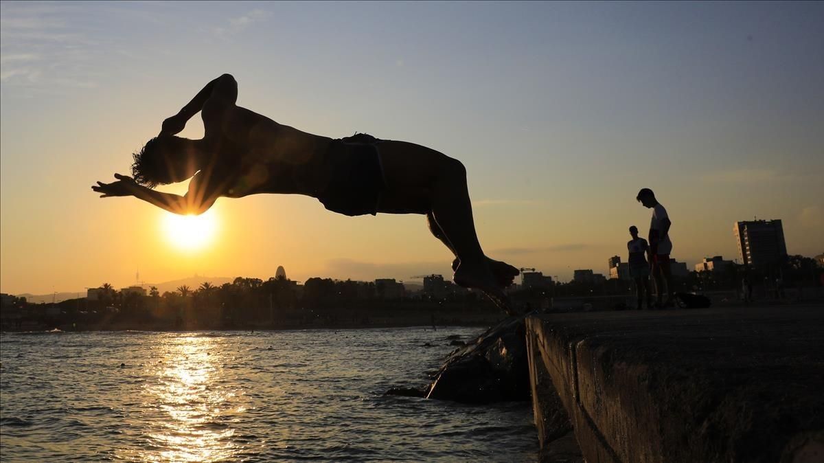 Un hombre salta al mar desde un espigón de la playa del Poblenou, en Barcelona. Un hombre salta al mar desde un espigón de la playa del Poblenou, en Barcelona.