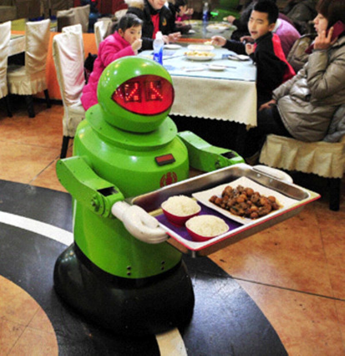 El androide sirve la comida ante la atenta mirada de unos niños.