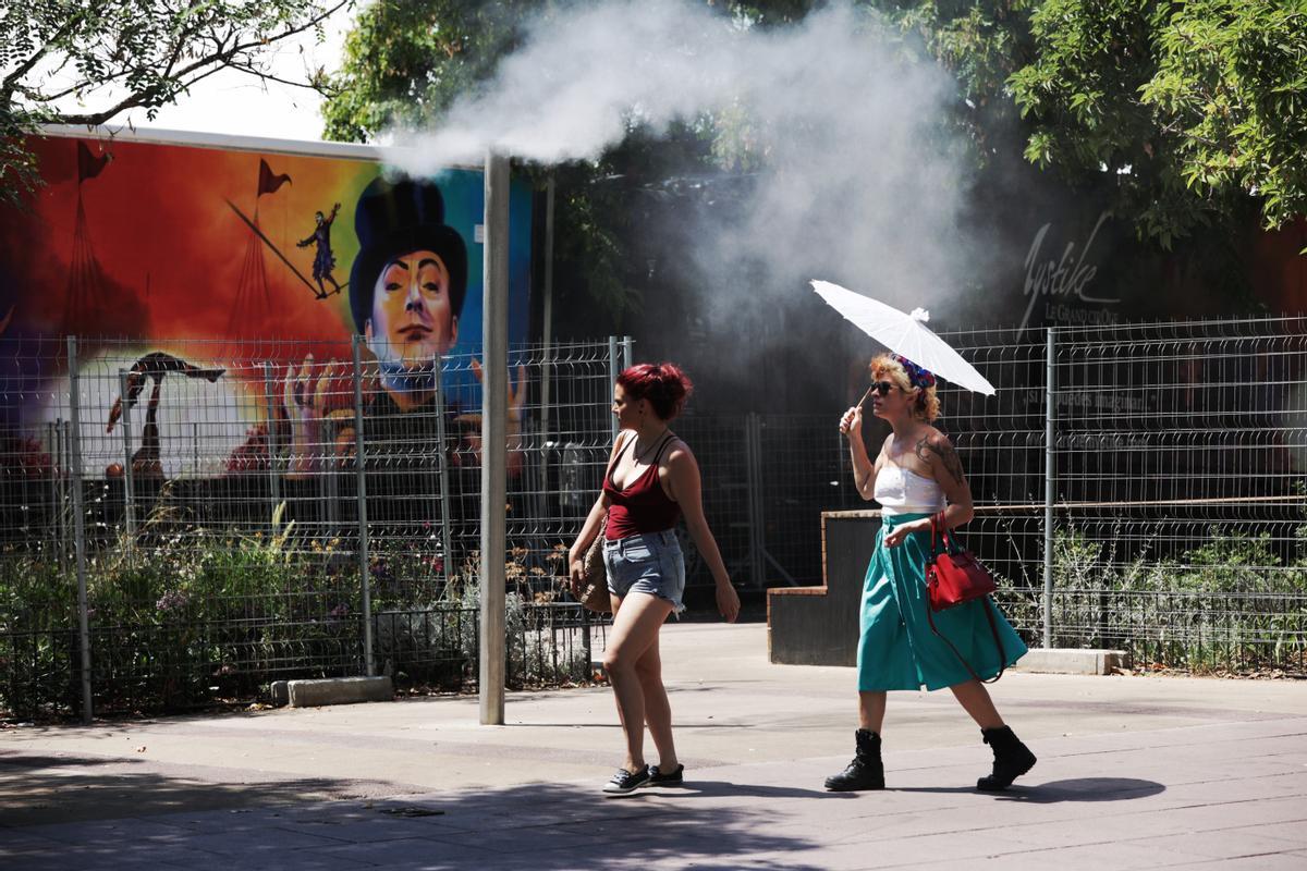 Unos turistas intentan refrescarse en unos vaporizadores de agua fresca instalados en los refugios climáticos del Passeig Joan de Borbó, en la Barceloneta.