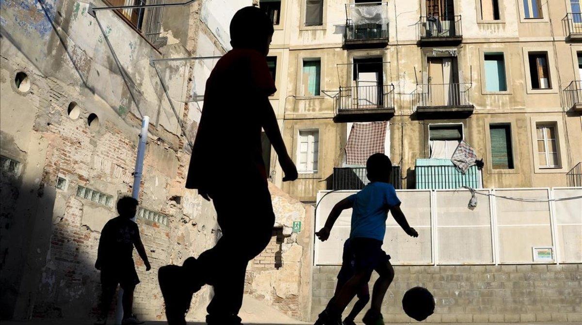 Varios niños juegan a fútbol en una pista del Raval, en Barcelona.