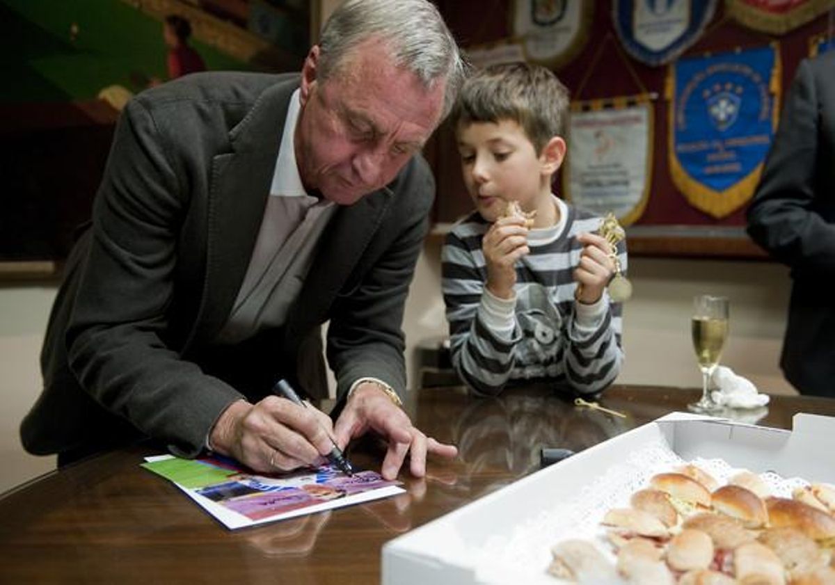 El seleccionador català Johan Cruyff firma un autògraf supervisat per un nen mentre menja uns canapès en la presentació de la selecció catalana que jugarà el dia 30 contra Tunísia . El seleccionador català Johan Cruyff firma un autògraf supervisat per un nen mentre menja uns canapès en la presentació de la selecció catalana que jugarà el dia 30 contra Tunísia .