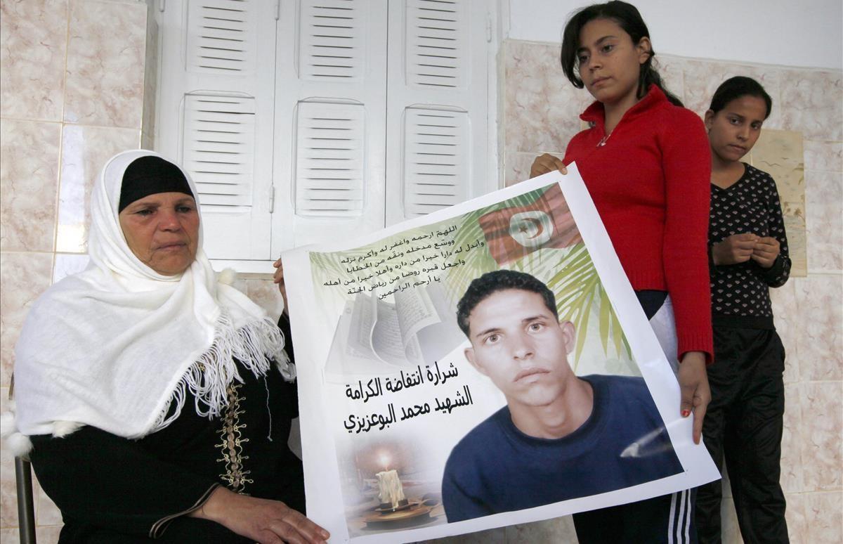 Manoubia Bouazizi sostiene un cartel con la imagen de su hijo junto a sus hijas Samia y Besma en su casa en el distrito de Marsa, en el norte de Túnez. Su hijo Mohamed se prendió fuego en un acto de protesta, hecho que inspiró la Primavera Árabe.   