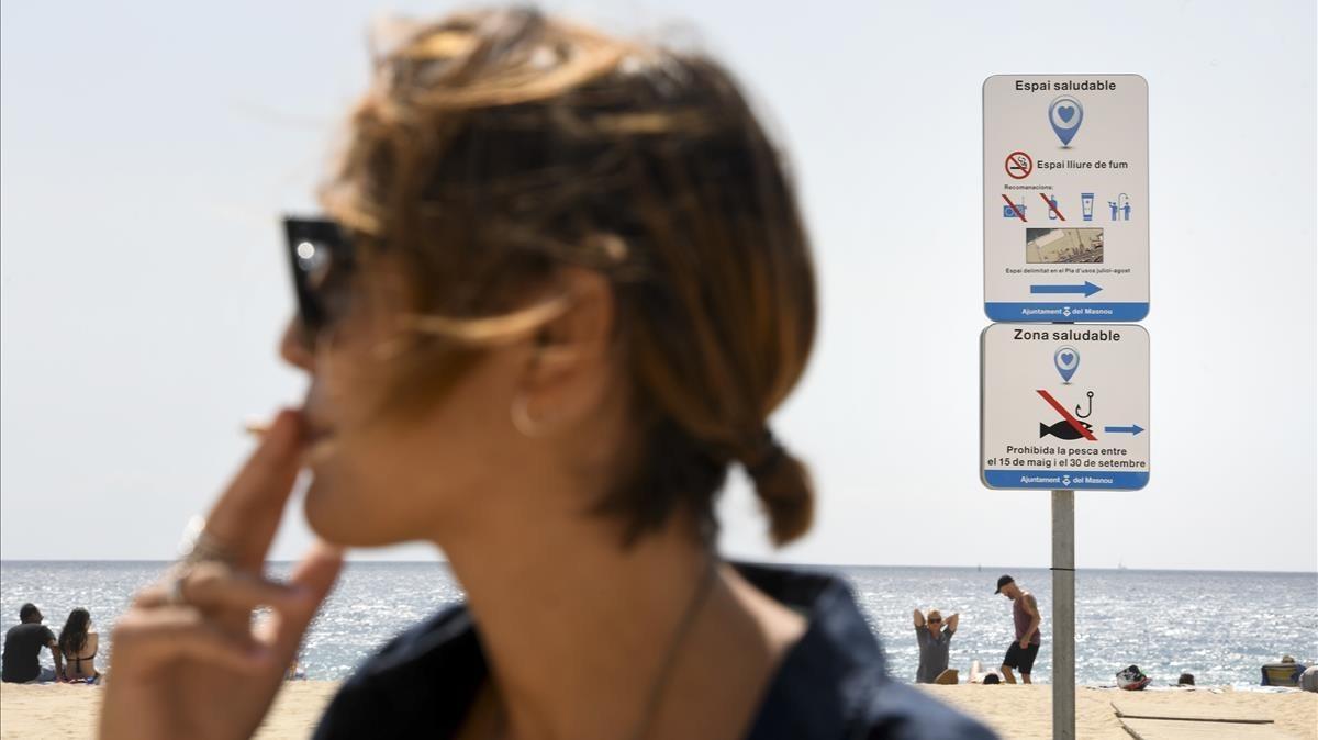 Una  joven da la última  calada a su cigarrillo antes de entrar en el espacio delimitado como libre de humo en la playa de El Masnou.