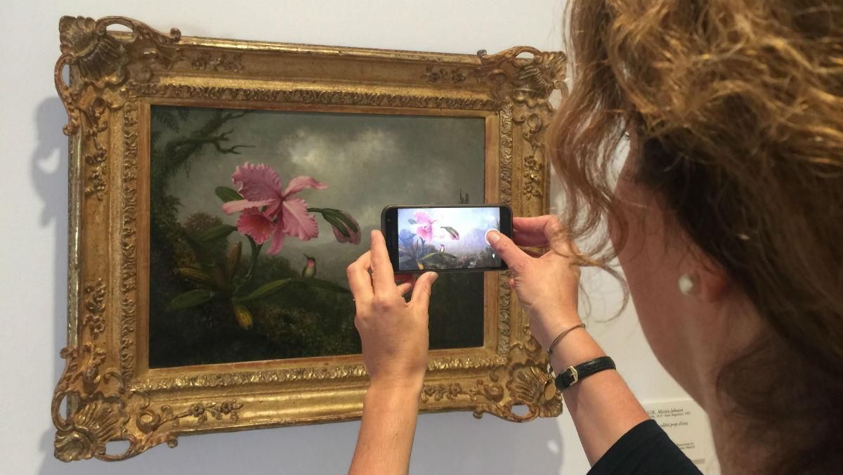 Una visitante fotografía ‘Orquídea y colibrí cerca de una cascada’ de Martin Johnson Heade, la obra de la exposición preferida de Carmen Thyssen. Una visitante fotografía ‘Orquídea y colibrí cerca de una cascada’ de Martin Johnson Heade, la obra de la exposición preferida de Carmen Thyssen.