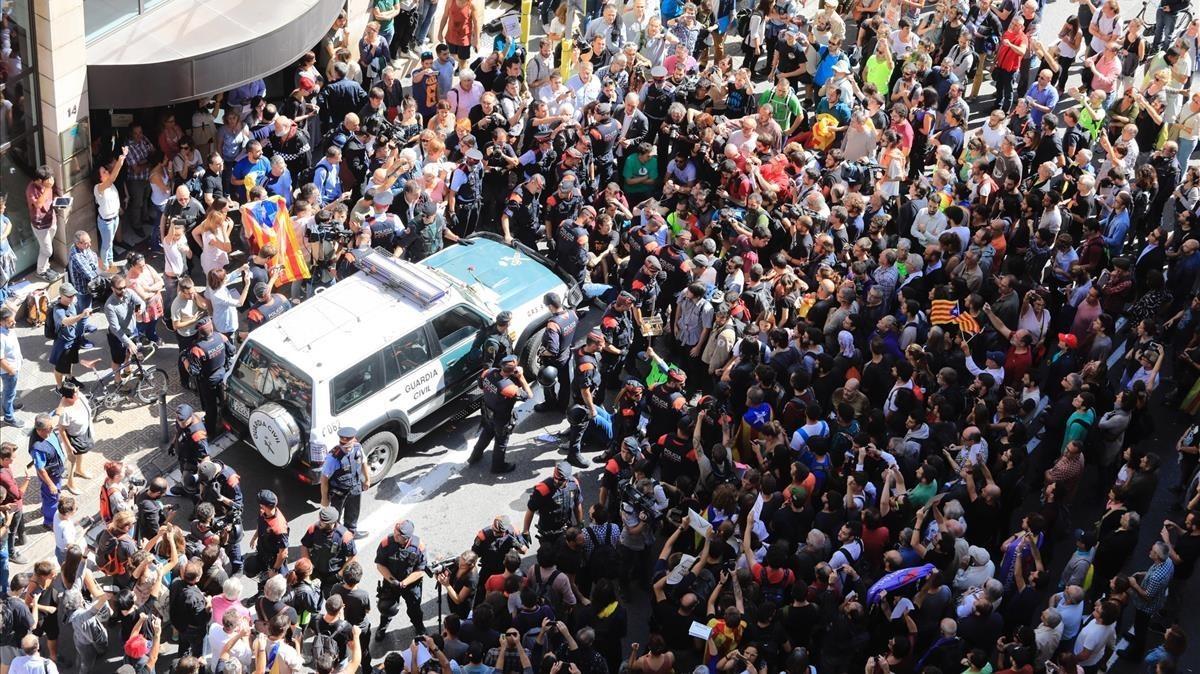 Decenas de personas intentan impedir que salga el coche de la Guardia Civil tras el registro al Departament d’Afers Exteriors de la Generalitat.