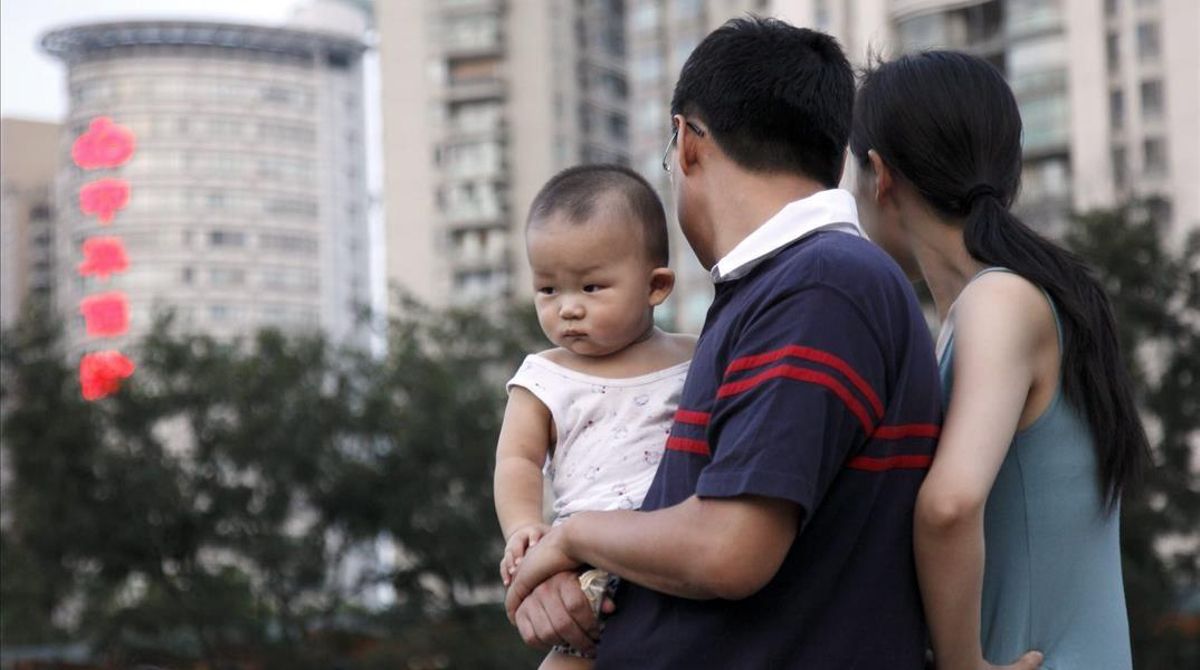 Una pareja observa a unos niños jugando en un parque cargando a su bebe en Shangai (China) Una pareja observa a unos niños jugando en un parque cargando a su bebe en Shangai (China)