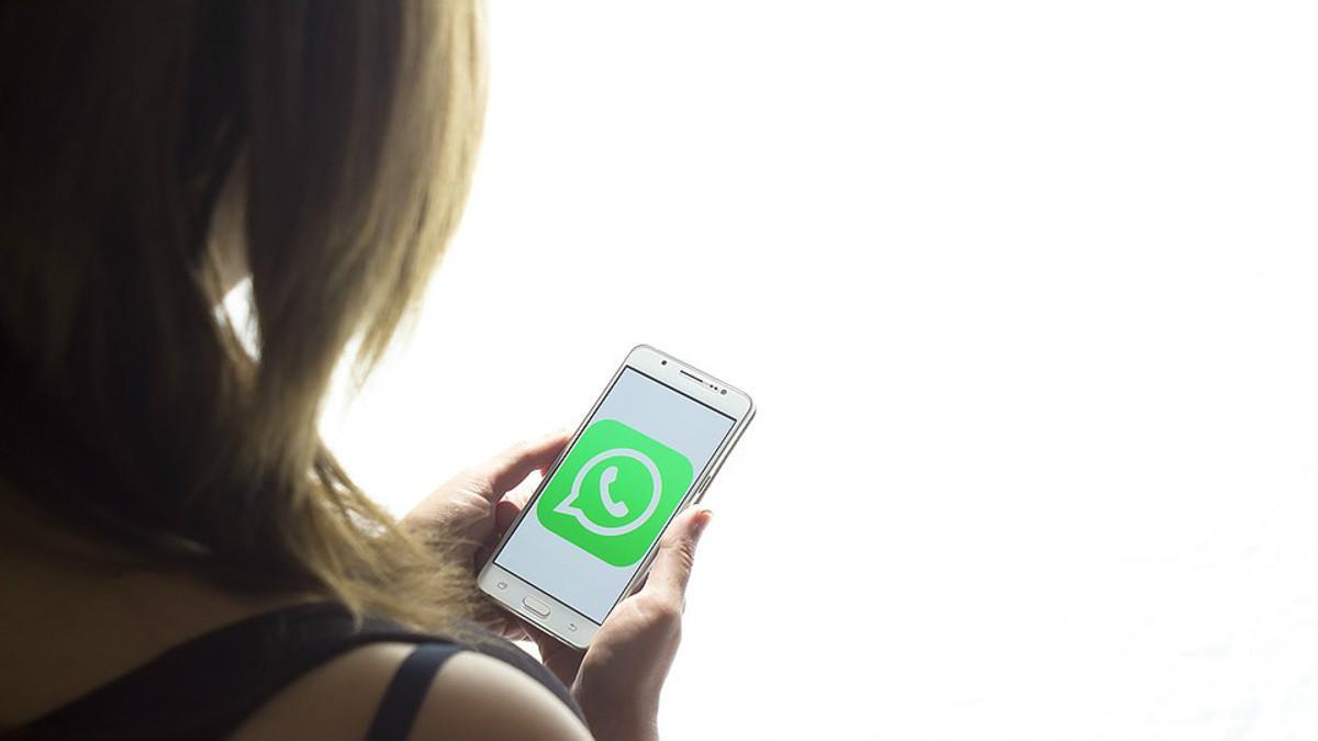 Una chica mira la pantalla de su teléfono móvil, con el logo de Whatsapp.