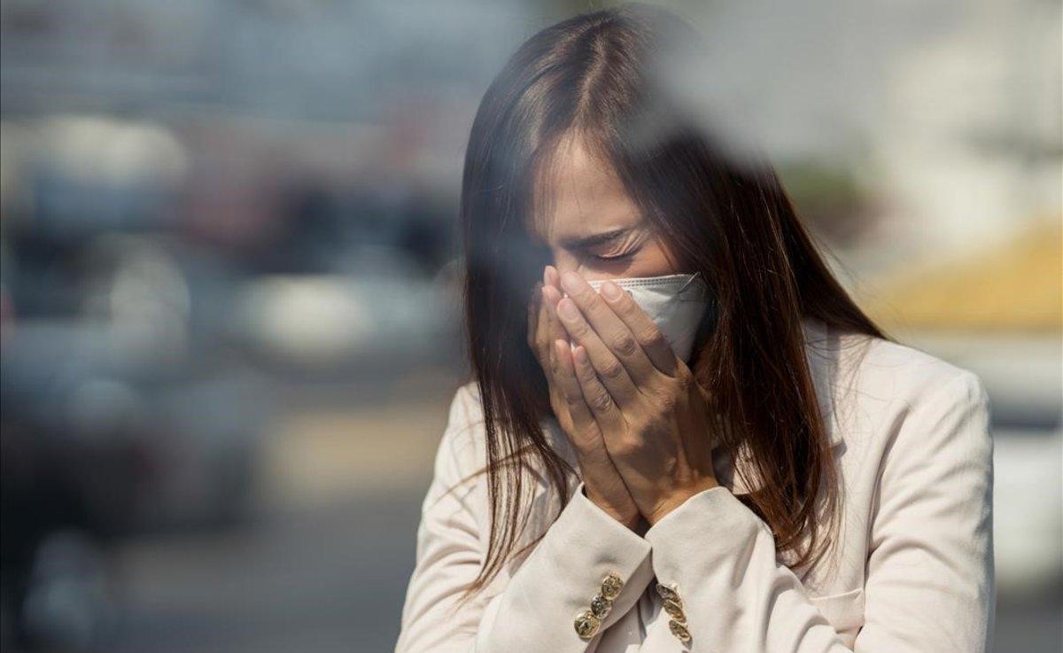 Una mujer con mascarilla estornuda.