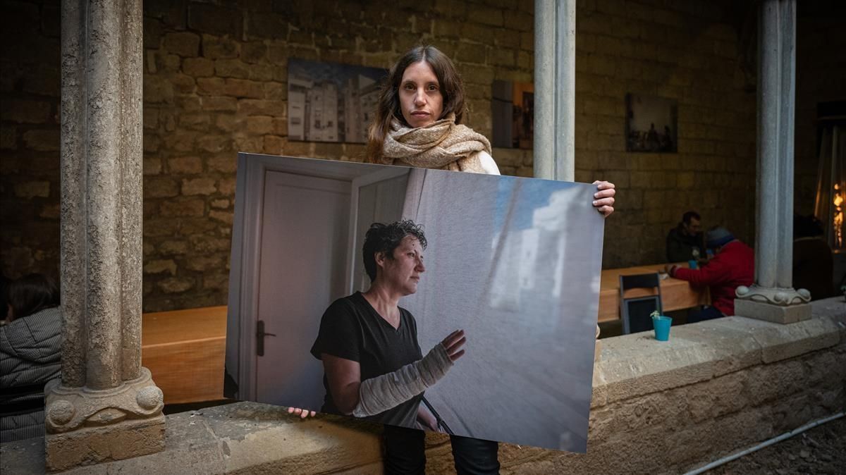 Maria Contreras Coll, en el claustro de Santa Anna con una de las imágenes de su exposición sobre la ayuda que ofrece la parroquia a los afectados por el covid-19.. Maria Contreras Coll, en el claustro de Santa Anna con una de las imágenes de su exposición sobre la ayuda que ofrece la parroquia a los afectados por el covid-19..