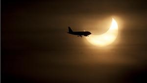 Un avión cruza el Sol eclipsado parcialmente por la Luna.