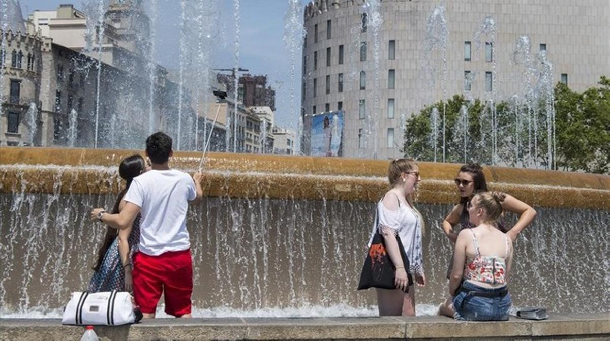 Unas personas se remojan en una fuente de plaza Catalunya este verano en plena ola de calor.