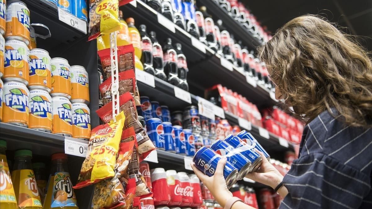 Una joven observa la etiqueta de un refresco en un supermercado Una joven observa la etiqueta de un refresco en un supermercado