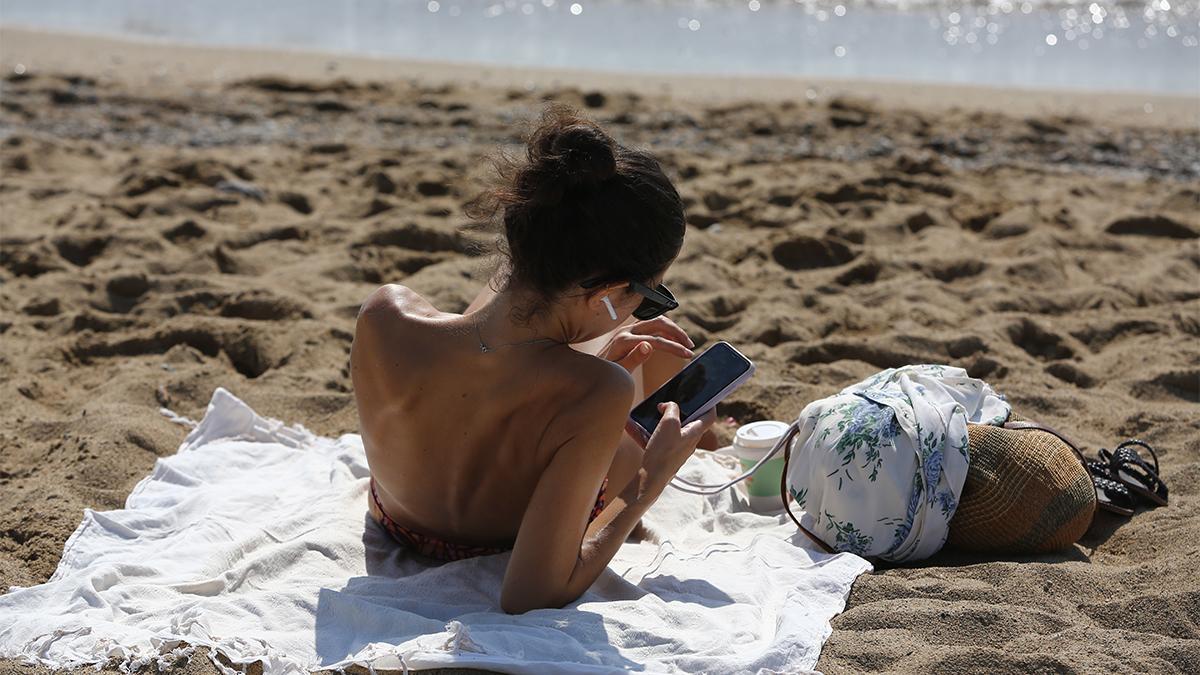 Desconexión del trabajo pero con el móvil, gente en la playa de la barceloneta con el móvil en la mano 