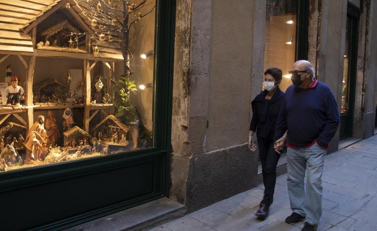 Una pareja con mascarilla pasea por el centro de Barcelona, frente a un establecimiento con motivos navideños. Una pareja con mascarilla pasea por el centro de Barcelona, frente a un establecimiento con motivos navideños.
