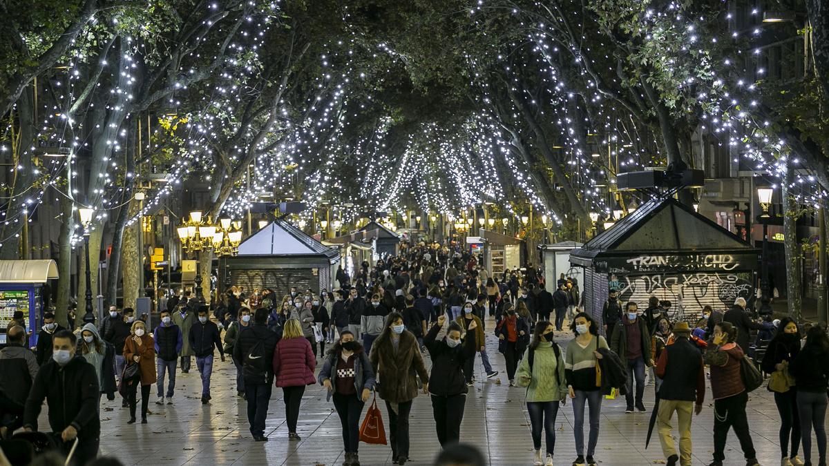 Transeúntes, la mayoría con mascarilla, en La Rambla de Barcelona iluminada para la Navidad.