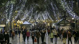 Transeúntes, la mayoría con mascarilla, en La Rambla de Barcelona iluminada para la Navidad.