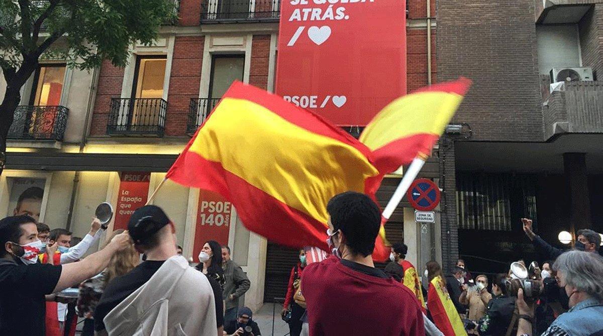 Un grupo de personas se manifiestan ante la sede del PSOE, protegida por la Policía Nacional, por la gestión de la crisis sanitaria, este domingo 17 de mayo.