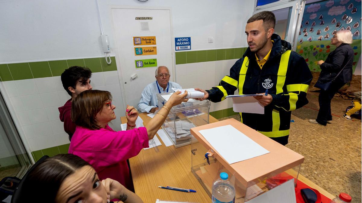 Un cartero entrega a la presidenta de una mesa electoral el voto por correo que corresponde a esa mesa, en el colegio de San José de Lorca.