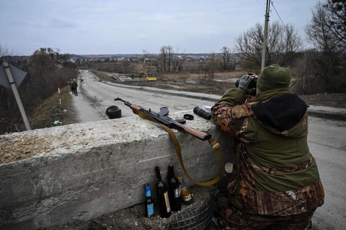 Un soldado ucraniano inspecciona el terreno con unos prismáticos, dirigiendo su atención hacia la ciudad de Stoyanka, en un puesto de control antes del último puente en la carretera que conecta esa población con Kyev.