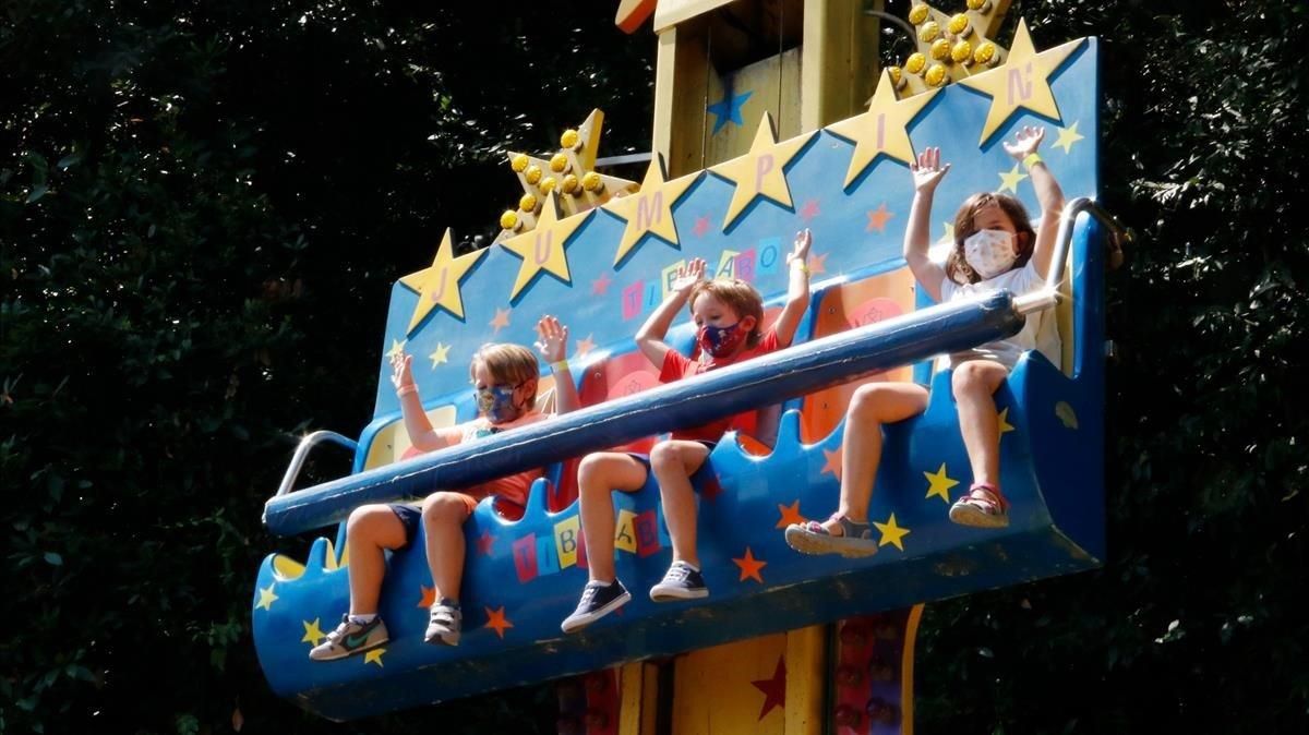 Tres niños con mascarilla disfrutan en una atracción del Tibidabo, el primer dia de su apertura. Tres niños con mascarilla disfrutan en una atracción del Tibidabo, el primer dia de su apertura.