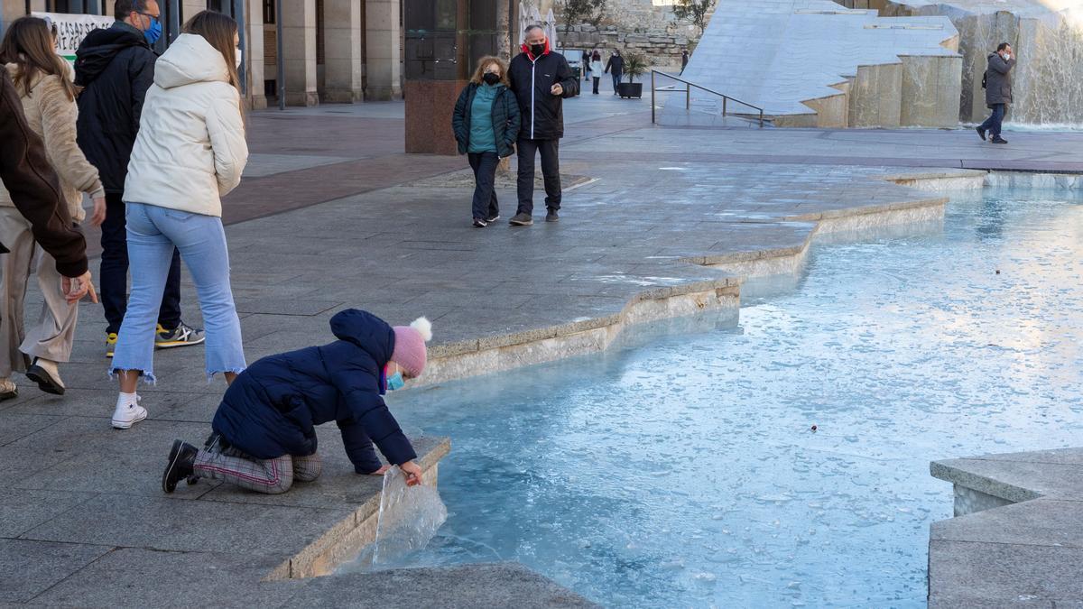 Una niña coge un trozo de hielo de una fuente helada en Zaragoza.  