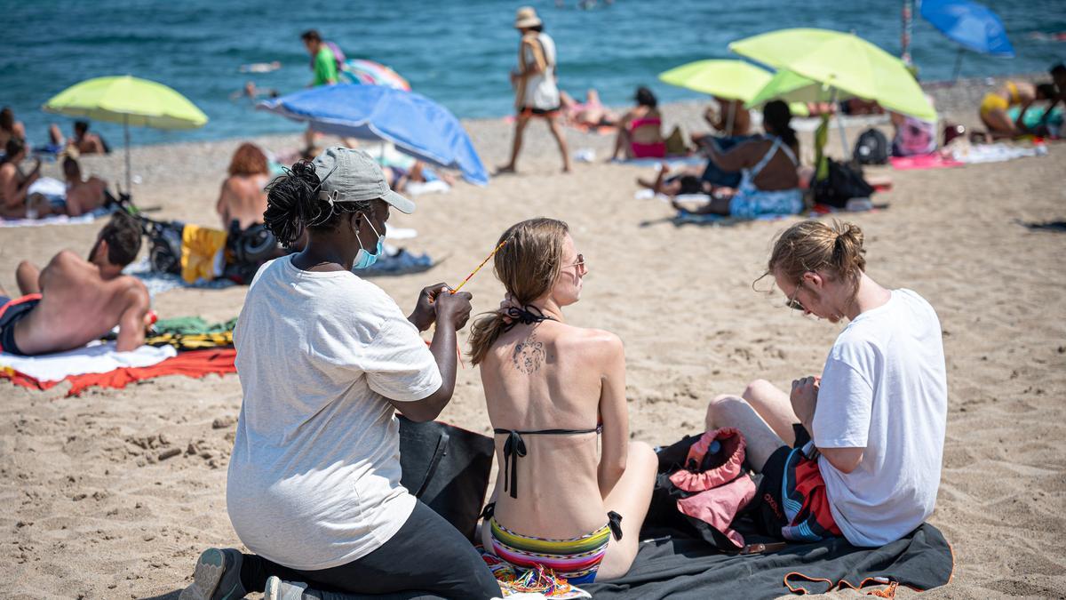 Una maliense le hace una trenza a una turista por tres euros, este jueves en la playa de la Barceloneta.