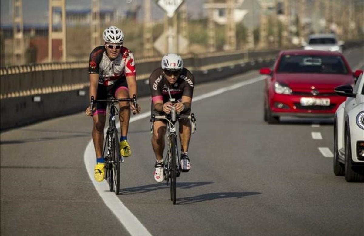 Dos ciclistas entrenan la mañana del viernes por la N-II, en Arenys de Mar, mientras los coches les pasan dejando un mínimo de 1,5 metros. 