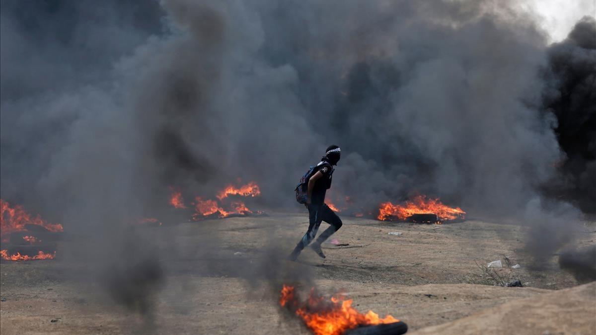 Un manifestante palestino corre entre las columnas de humo de neumáticos quemados en las protestas palestinas en la frontera de Gaza e Israel por el traslado de la embajada estadounidense a Jerusalén.