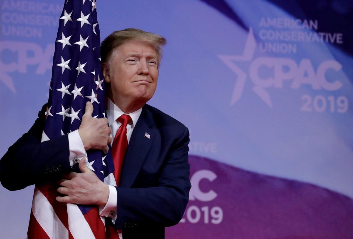 FILE PHOTO  U S  President Donald Trump hugs American flag at the Conservative Political Action Conference  CPAC  annual meeting at National Harbor near Washington  U S   March 2  2019  REUTERS Yuri Gripas File Photo
