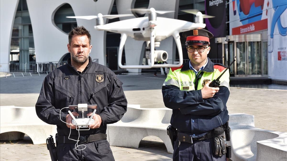 Dos de los agentes de la policía autonómica, el operador del dron (izquierda) y el radiofonista, realizan una demostración de vuelo delante del recinto ferial donde se celebrará el Mobile, este jueves. 