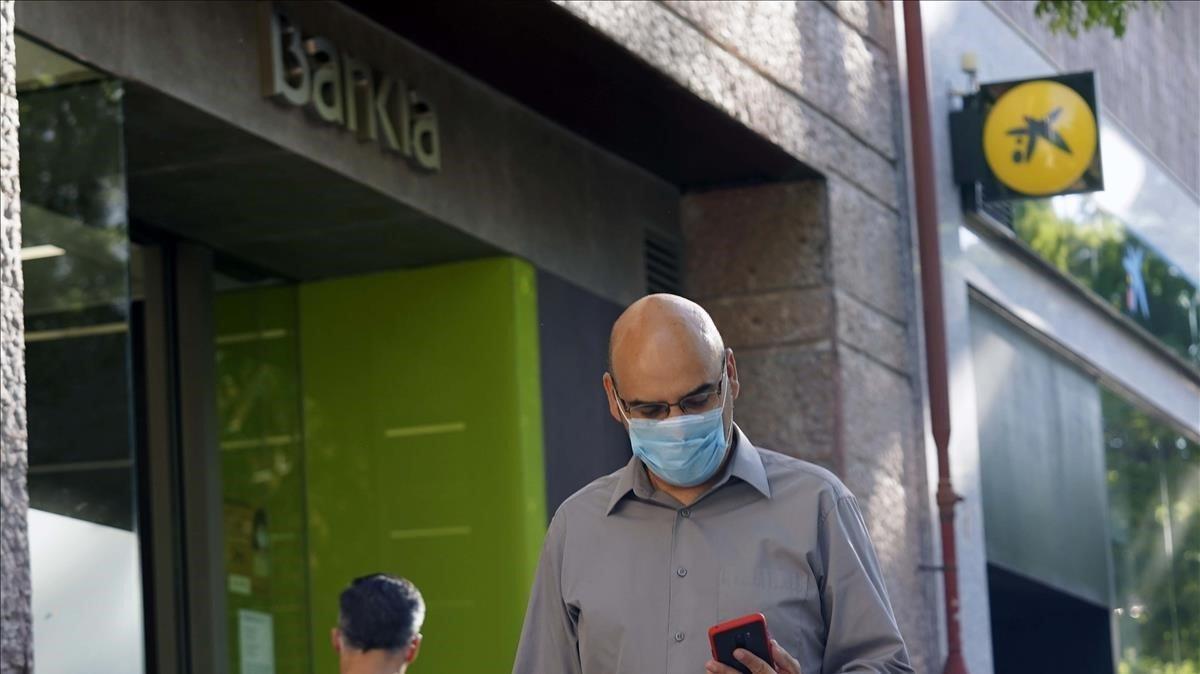 Un hombre camina delante de dos oficinas contiguas de Bankia y CaixaBank.