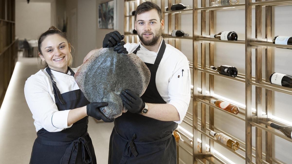 Lena María Grané y Ricky Smith, con un rodaballo en la entrada del restaurante Baló. Lena María Grané y Ricky Smith, con un rodaballo en la entrada del restaurante Baló.