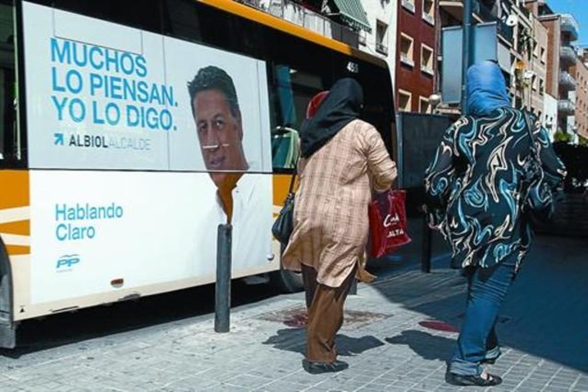 Dos inmigrantes pasan junto a un autobús con una pancarta de campaña de Albiol en el barrio de la Salut de Badalona, el pasado 18 de mayo. Dos inmigrantes pasan junto a un autobús con una pancarta de campaña de Albiol en el barrio de la Salut de Badalona, el pasado 18 de mayo.