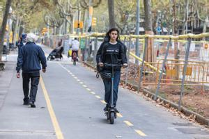 Una usuaria de patinete eléctrico, sin el casco puesto, por una calle de Barcelona