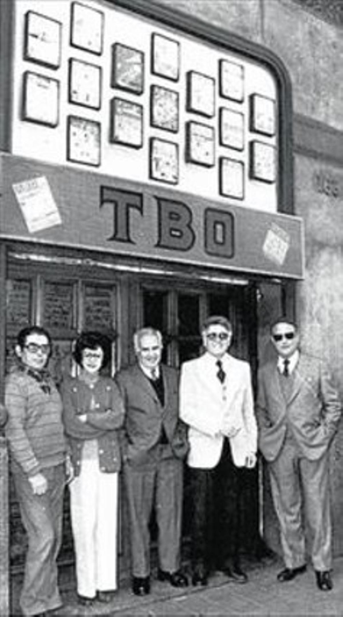 Hoy y ayer 8Rosa Segura, con un antiguo ejemplar del ’TBO’ en su casa (arriba). Abajo, en 1983, en la puerta de la revista, con el director, Albert Viña (americana blanca), y el guionista Carles Bech (gafas de sol).