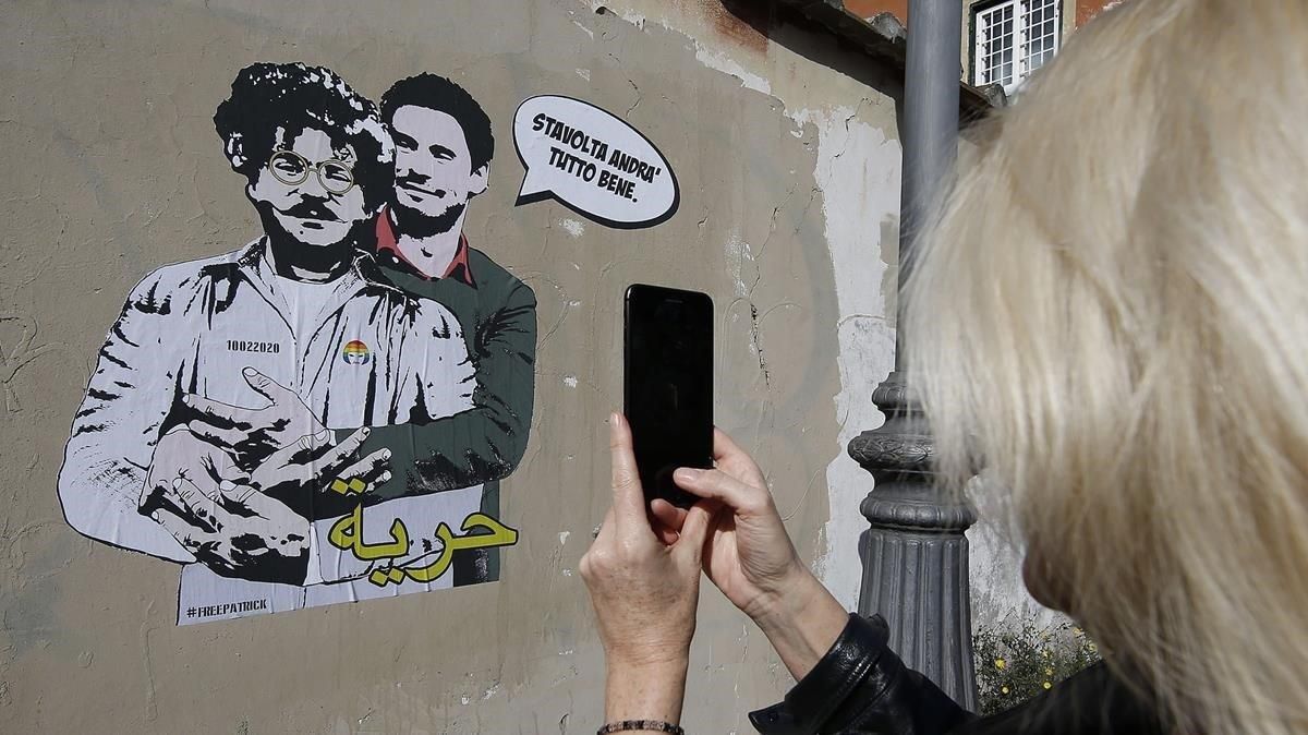 Una mujer toma una fotografía de un mural con las imágenes de Patrick George Zaki (izquierda) junto a Giulio Regeni, cerca de la embajada de Egipto en Roma. Una mujer toma una fotografía de un mural con las imágenes de Patrick George Zaki (izquierda) junto a Giulio Regeni, cerca de la embajada de Egipto en Roma.