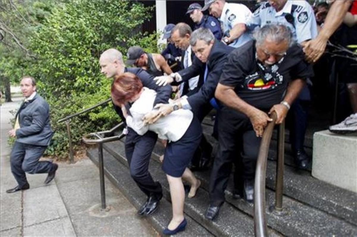 Los policías sacan en volandas a la primera ministra de Australia, tras ser abucheada por aborígenes, el jueves, en Canberra.