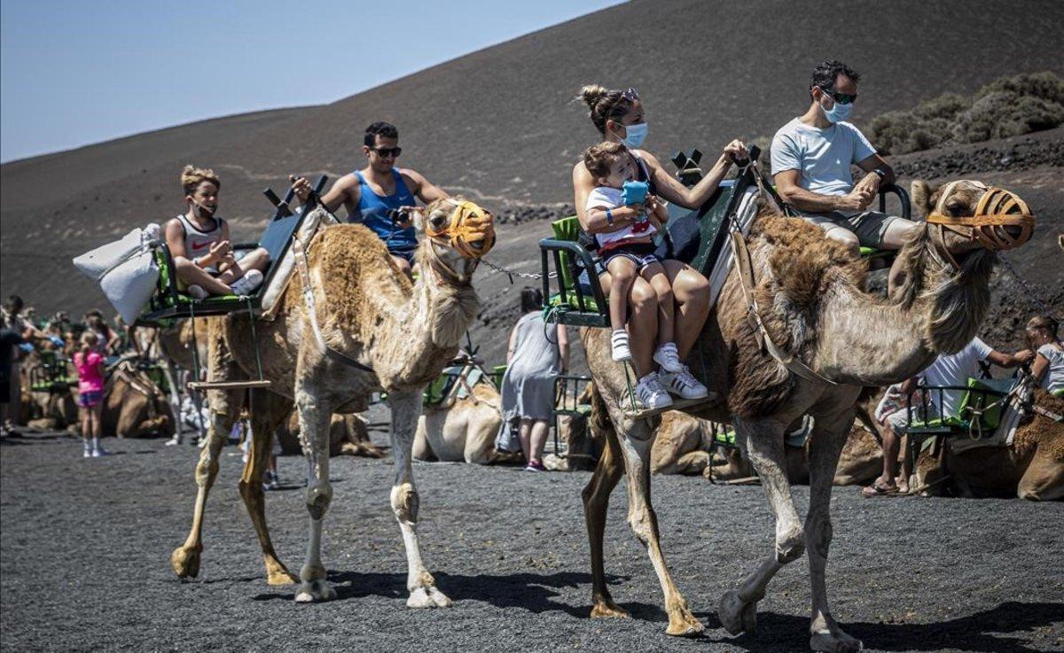 Turistas, protegidos con mascarillas, en camello por el Parque Nacional de Timanfaya, en Lanzarote.