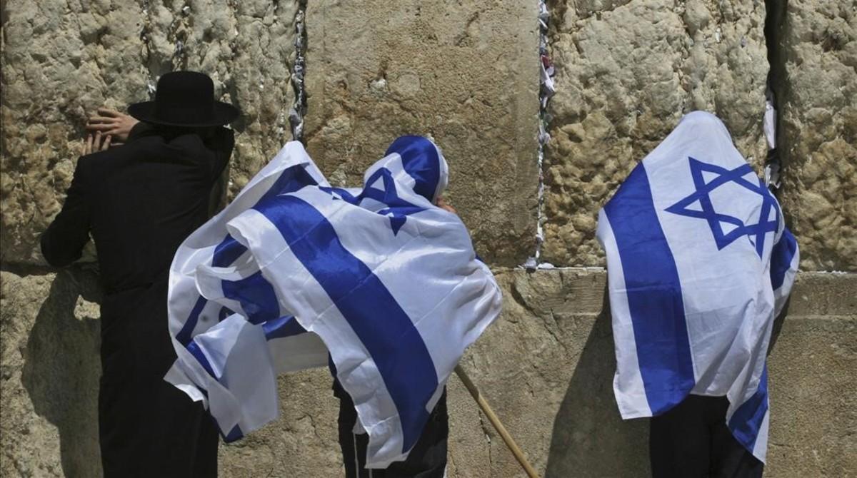 Jóvenes israelís se cubren con la bandera de Israel junto a un untraortodoxo frente al Muro de las Lamentaciones.