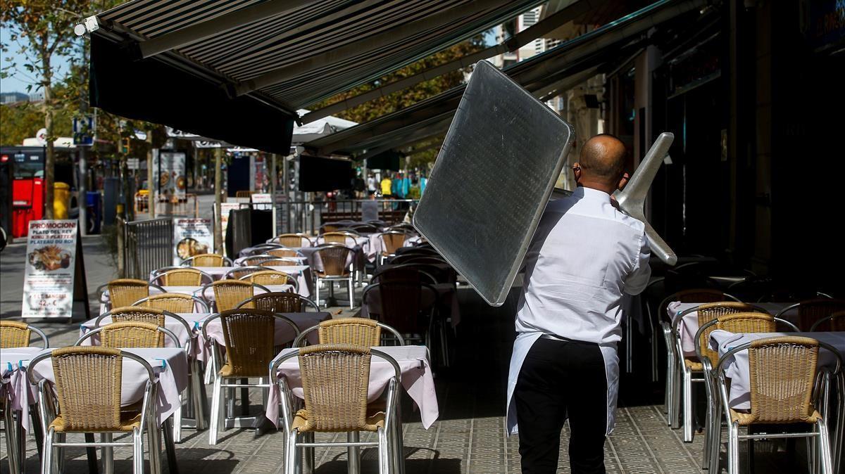 Un camarero recoge una mesa de una terraza de un restaurante del barrio de la Barceloneta. 