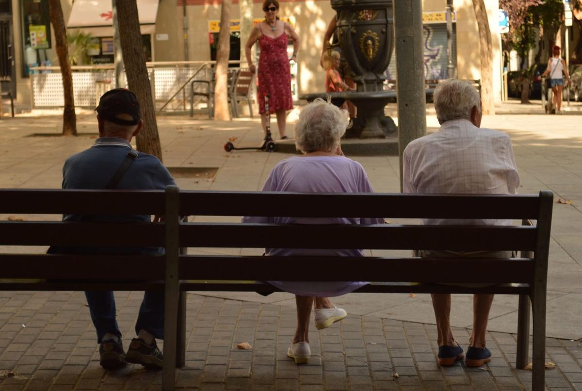 Tres pensionistas descansan en un banco en la plaza del surtidor de Poble Sec, en Barcelona.