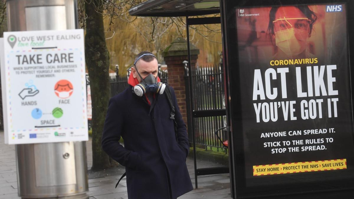 Un hombre, ataviado con una máscara antigás, pasa al lado de un cartel gubernamental para prevenir el contagio de coronavirus, este martes.